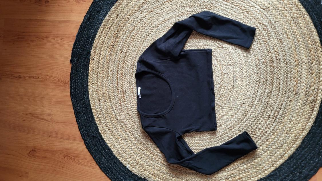 Black long-sleeved top on a round jute rug with dark edges, on a light wooden floor.