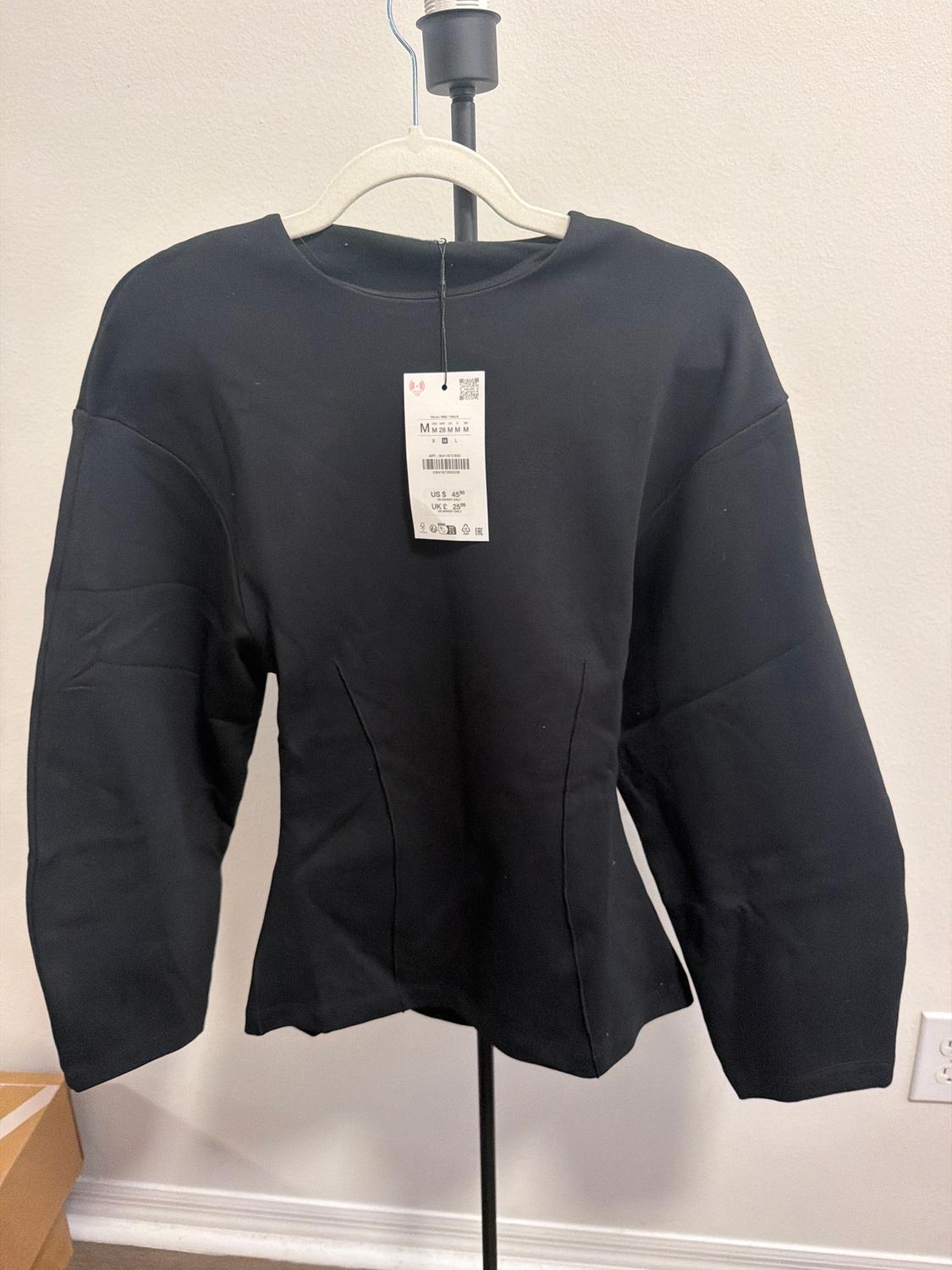 Black long-sleeved jersey on a hanger, with a visible tag showing size and price. White background and cardboard box on the floor.