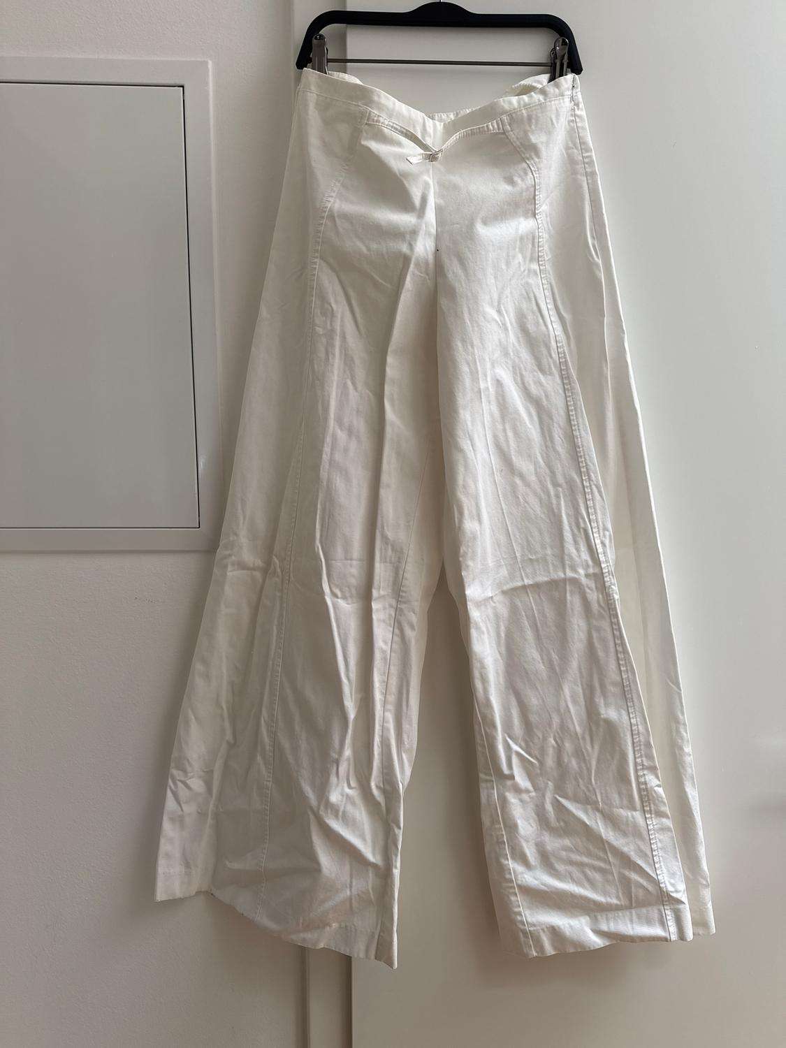 White, wide-leg trousers hanging on a black hanger over a white door. White wall background.