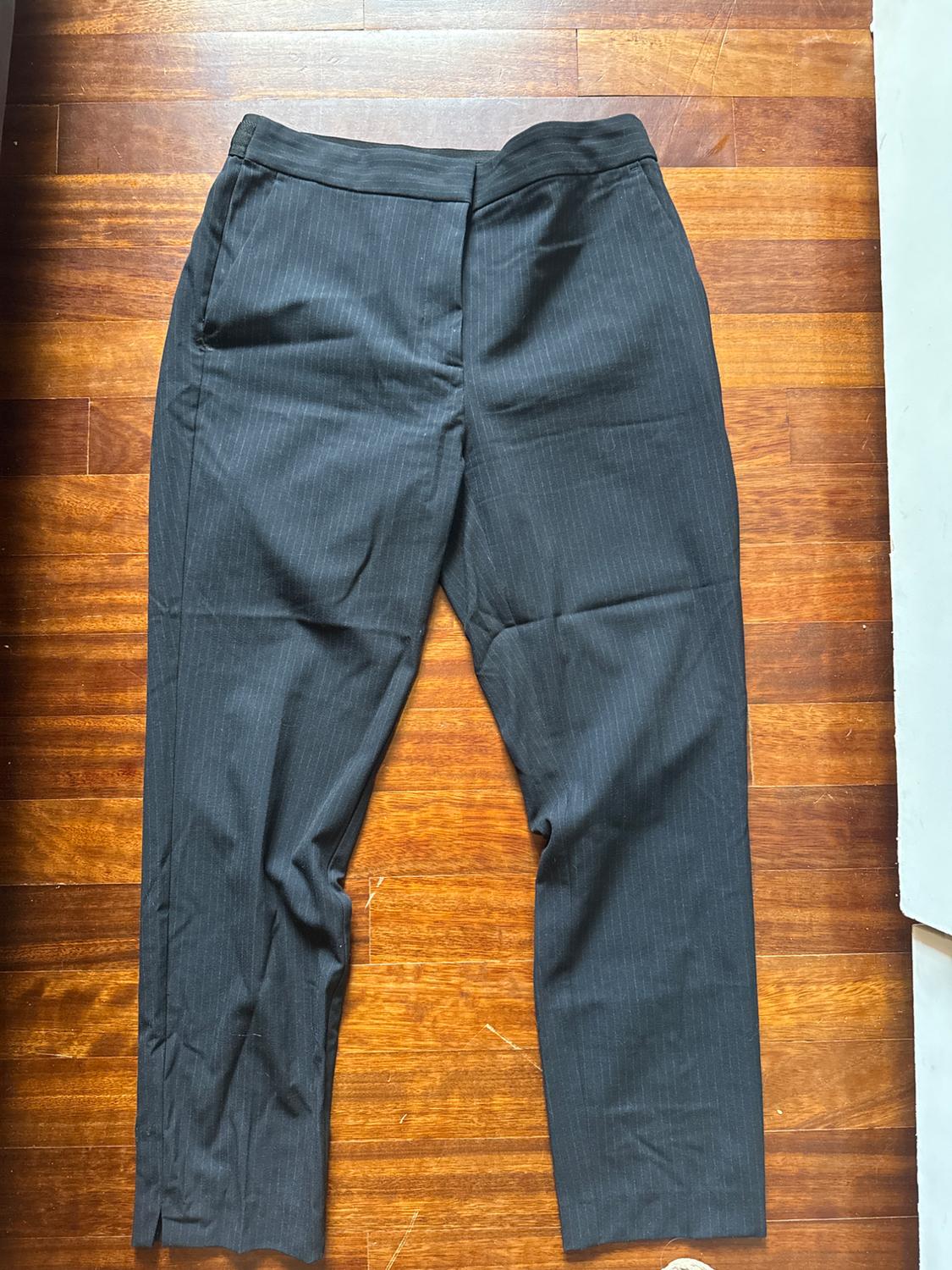 Black dress trousers with fine vertical stripes on a brown wooden floor.