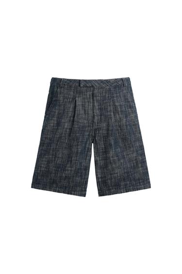 Dark blue textured Bermuda shorts with front pleats, side pockets, and belt loops, on a white background.