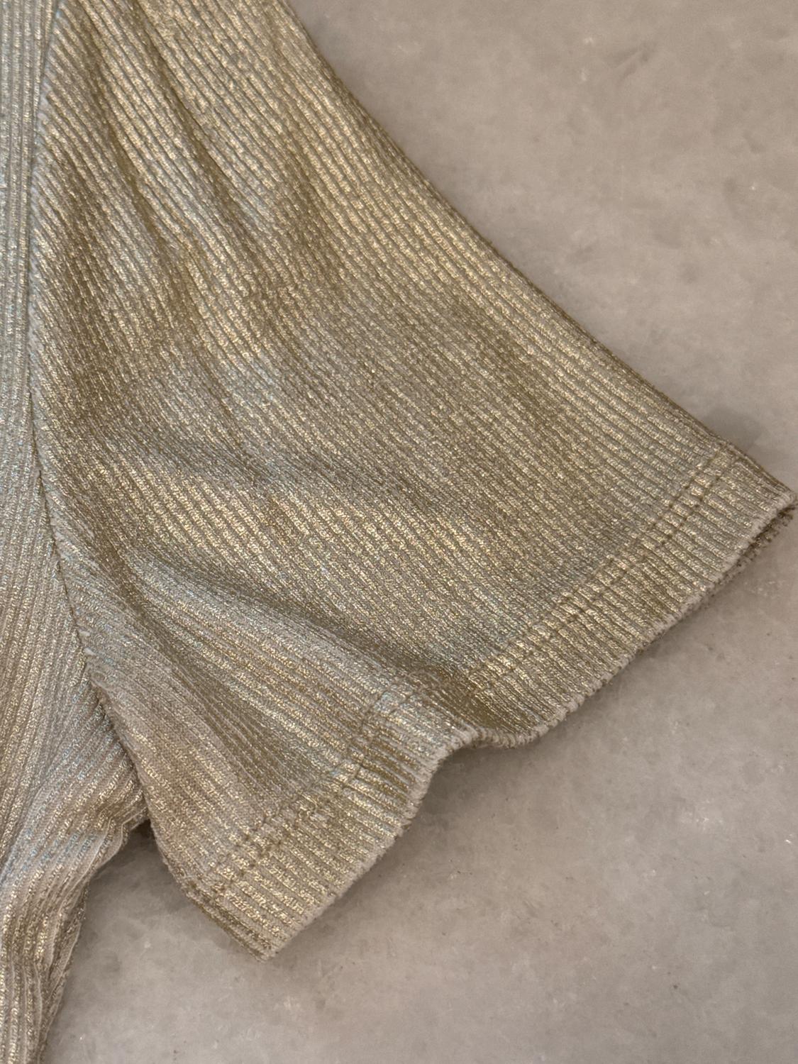 Golden ribbed textured fabric on a light gray background. The image shows a detail of a garment sleeve.