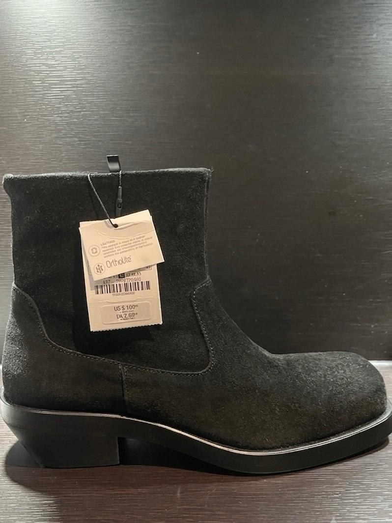 Black suede boot on a wooden background. It has tags with the text LEATHER, Ortholite and US $100.00.