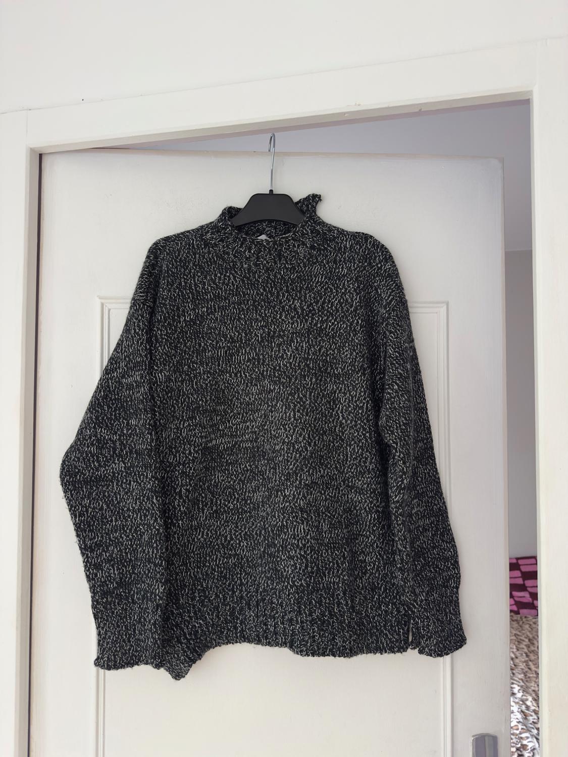 Dark grey chunky knit jumper hung on a white door with a black hanger. Minimalist and relaxed atmosphere.