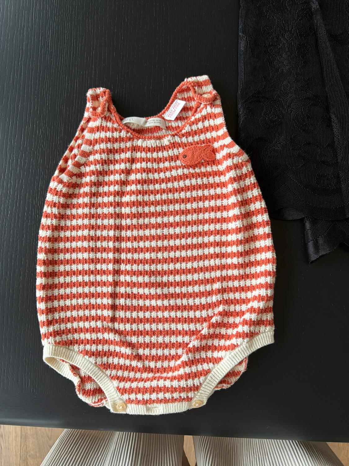 A striped jumper with orange and white stripes, with a fish on a dark table. The text reads: KEEP AWAY FROM FIRE.