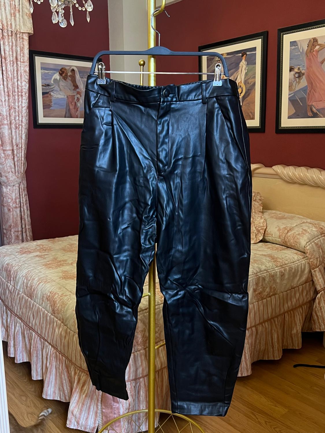 Black trousers hanging on a gold clothes rack in a bedroom with red walls and framed pictures. Bed with a patterned bedspread.
