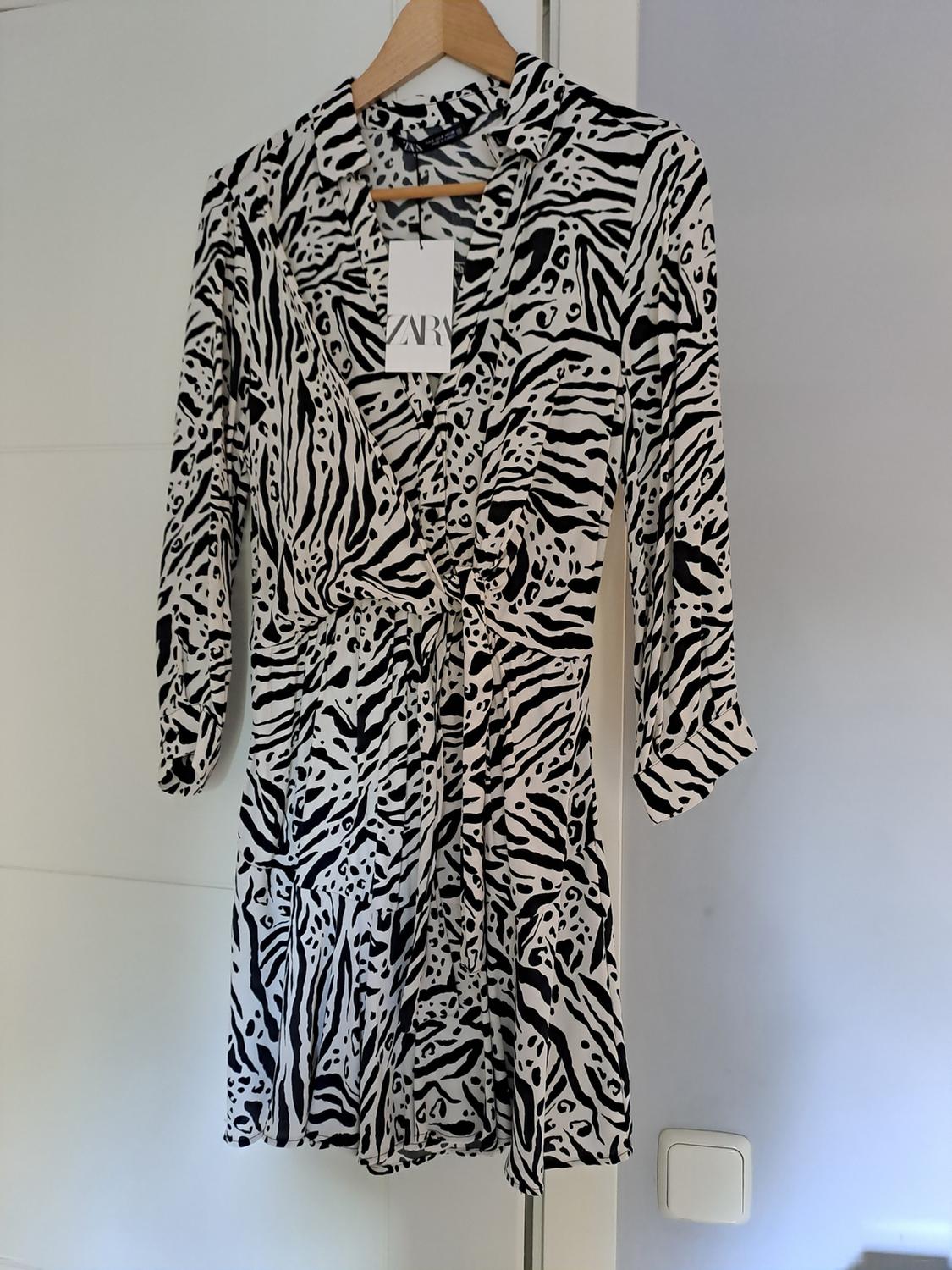 Black and white long-sleeved short animal print dress hanging on a door. Label visible with the text ZARA.