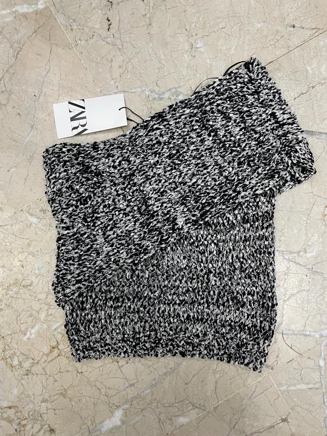 Black and white knitted scarf on a light marble floor. Visible label with the text "ZARA".