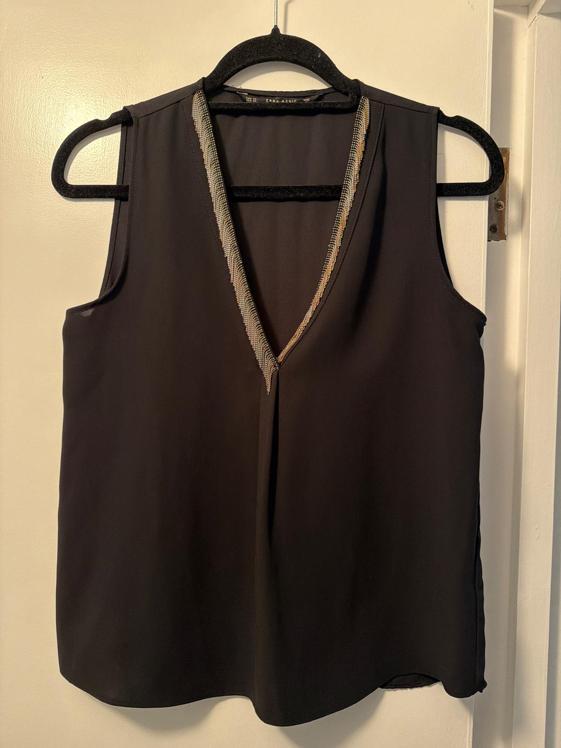 Black sleeveless V-neck top adorned with sparkling beads, hanging on a black hanger over a white door.