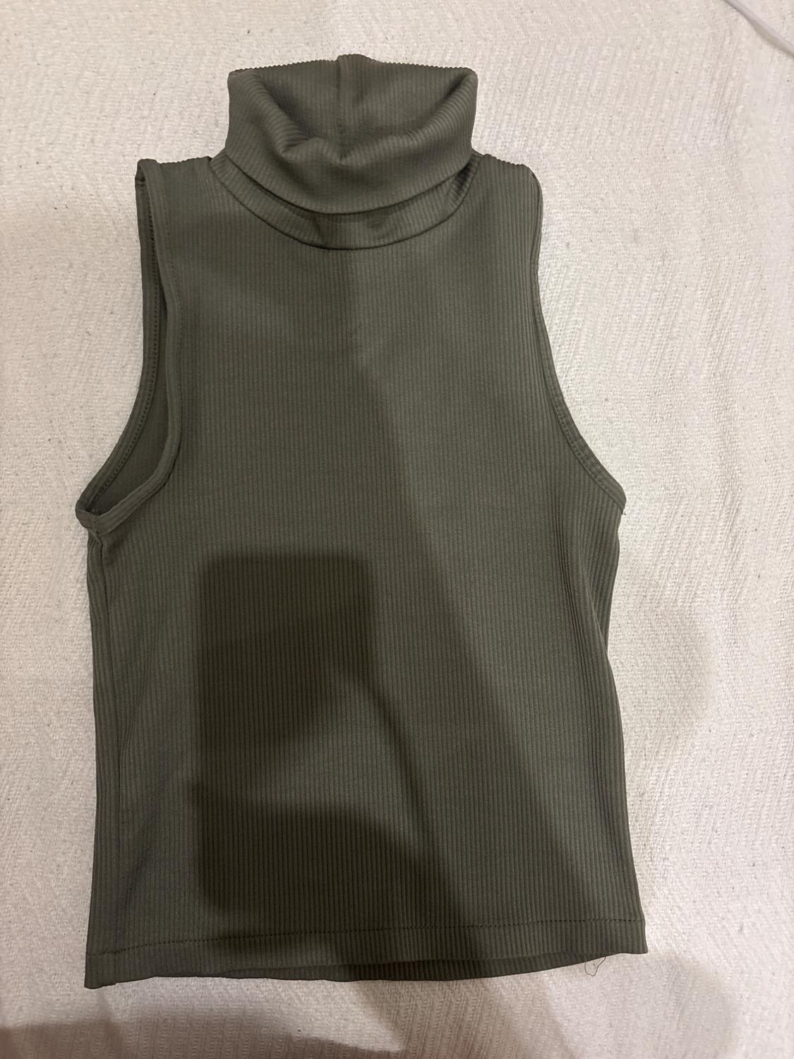 Olive green ribbed sleeveless top with a high neck, over a textured beige surface.