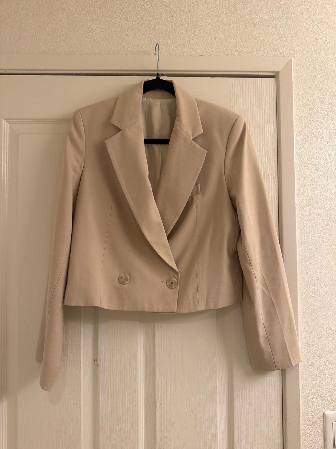 Beige double-breasted jacket hanging on a white door. Classic style with wide lapels and a straight cut.