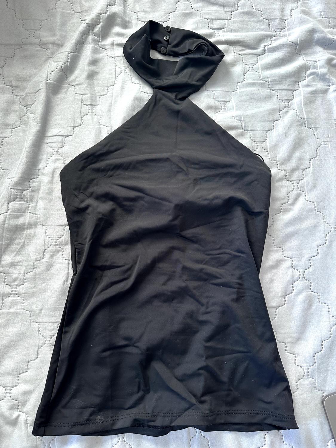 Black sleeveless halter neck top with button fastening, on a white bedspread with a diamond pattern.