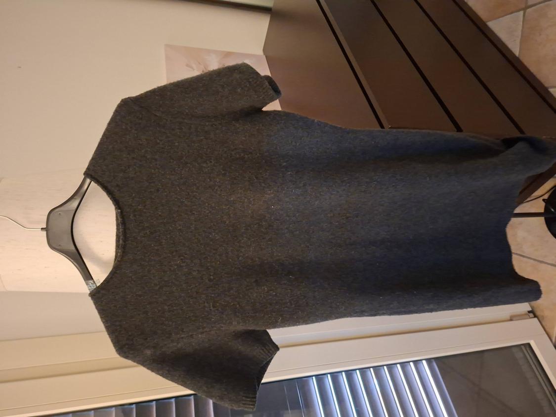 Grey short-sleeved jumper hanging on a black hanger, against a background of furniture and blinds.