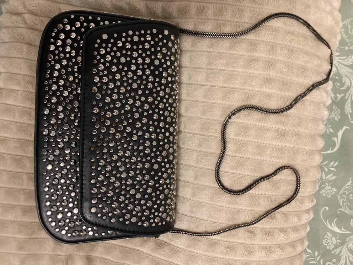 Black bag with silver studs and chain strap on a beige padded surface.