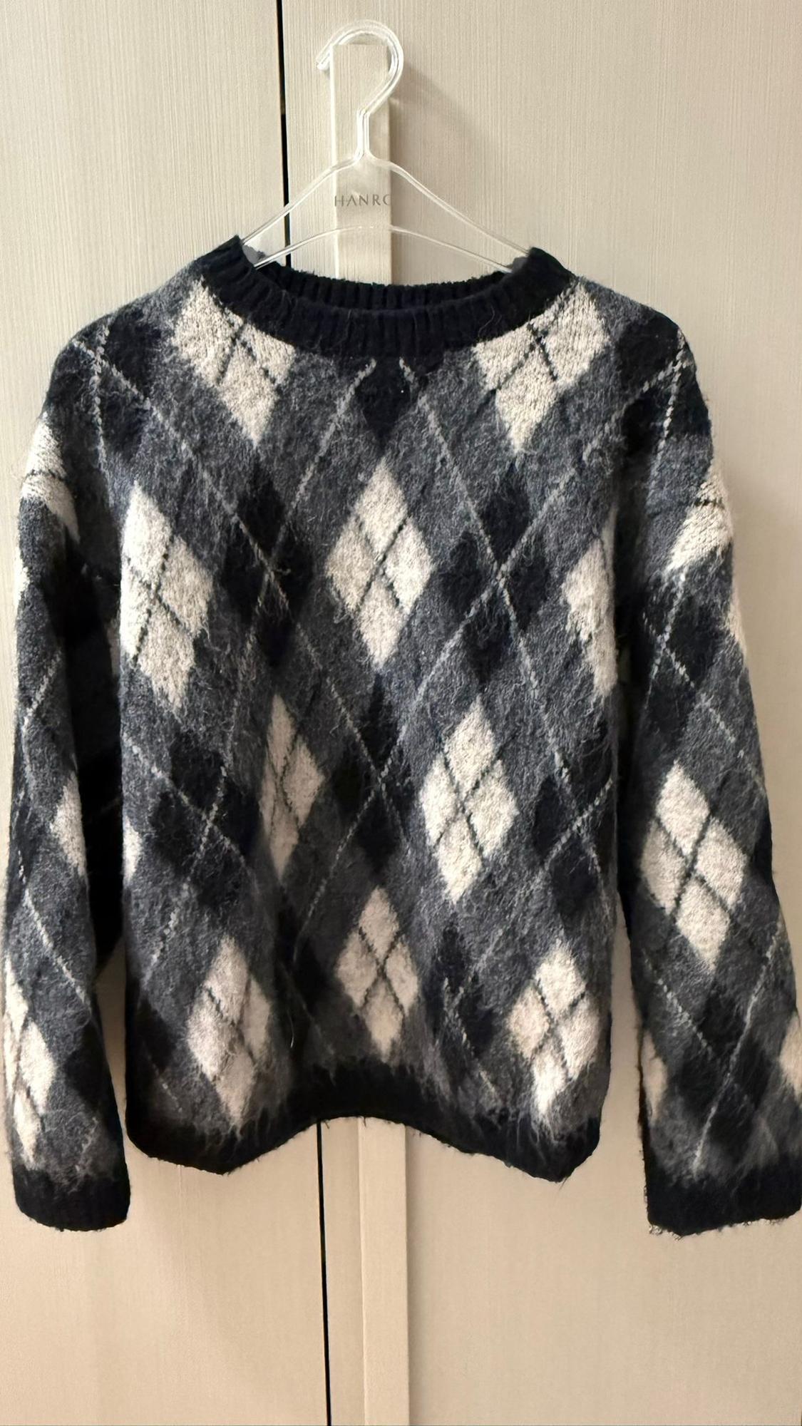 Black and white checked jumper hanging on a clear hanger. Beige wardrobe doors in the background.