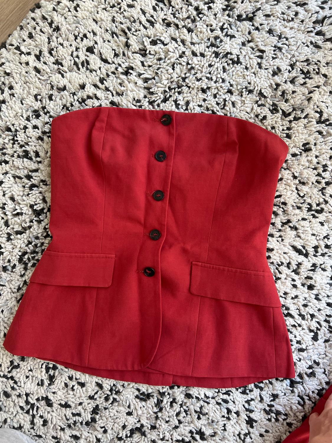 Red corset with black buttons on a thick-textured black and white rug.