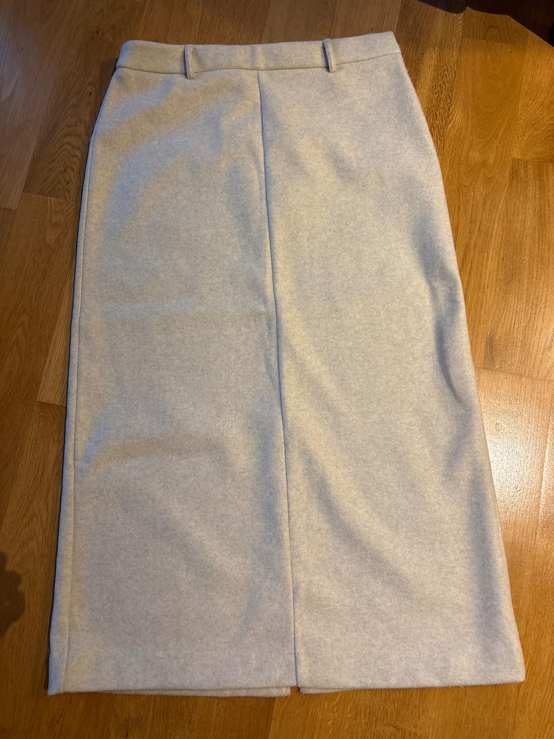 Light grey long skirt on a wooden floor, with a central pleat and belt loops.