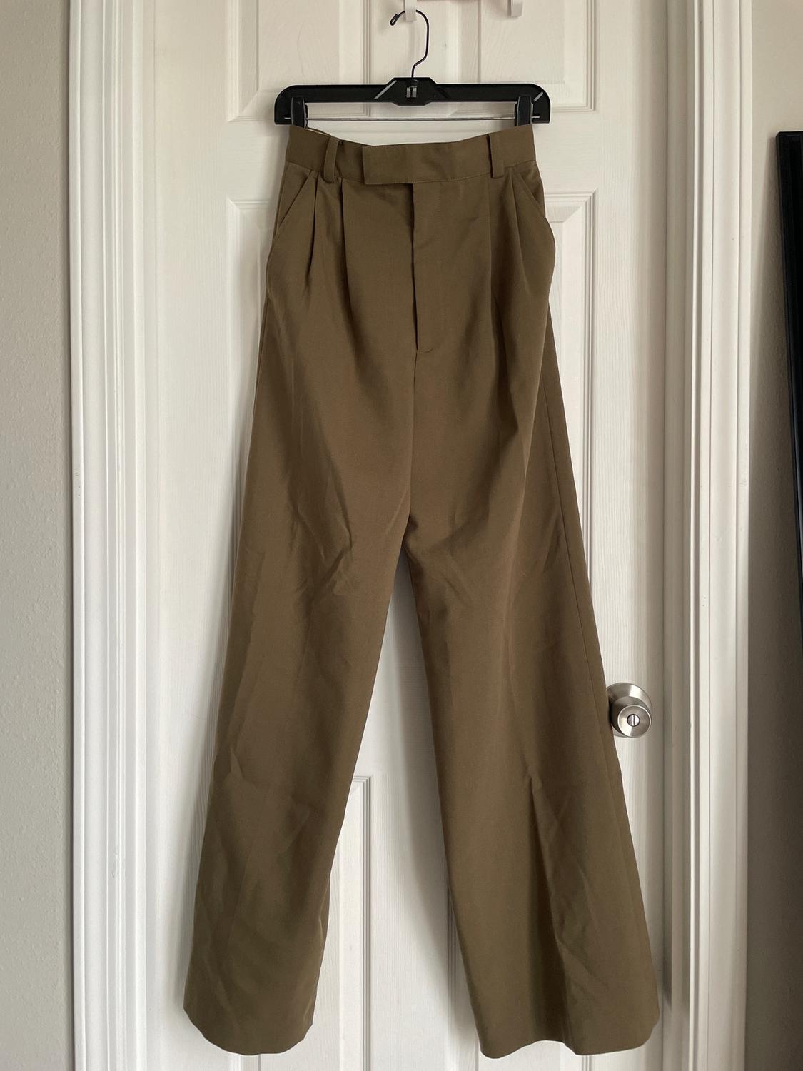 Brown wide-leg trousers hanging on a black hanger over a white door.