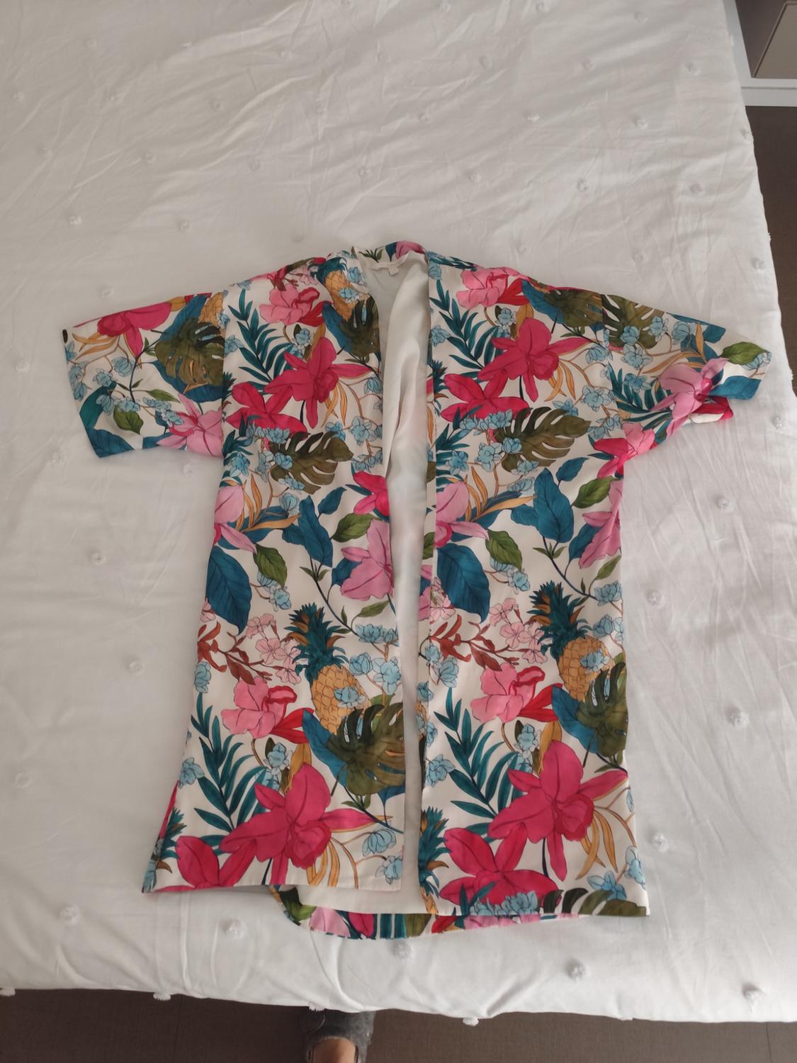 Colourful kimono with a floral and pineapple print on a white bed. Lightweight fabric and vibrant tropical design.