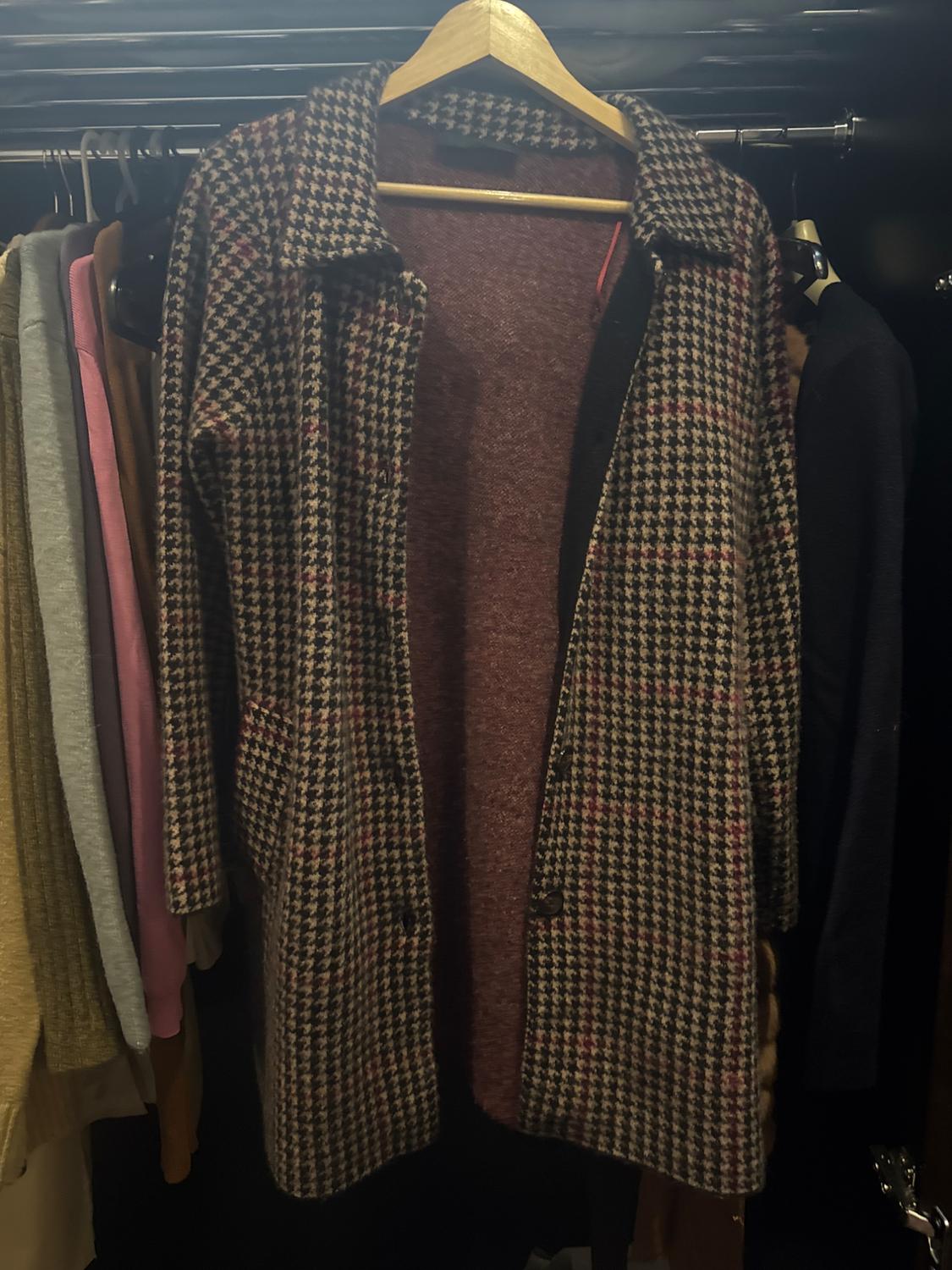 Brown and pink checked coat hanging on a clothes rail, surrounded by other garments in a dark wardrobe.