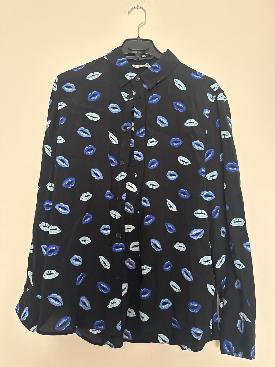 A black shirt with a lip design in blue and white tones, hanging on a hanger against a beige background.