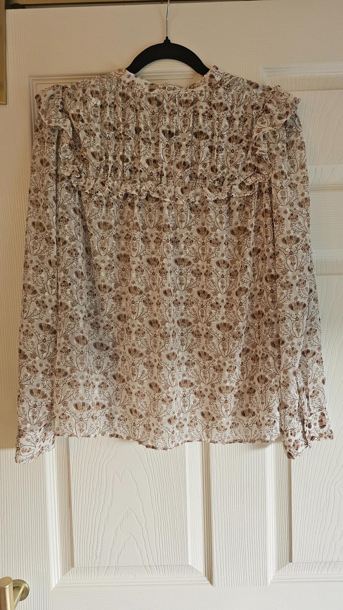 Brown and beige floral print long-sleeved blouse, hanging on a black hanger over a white door.