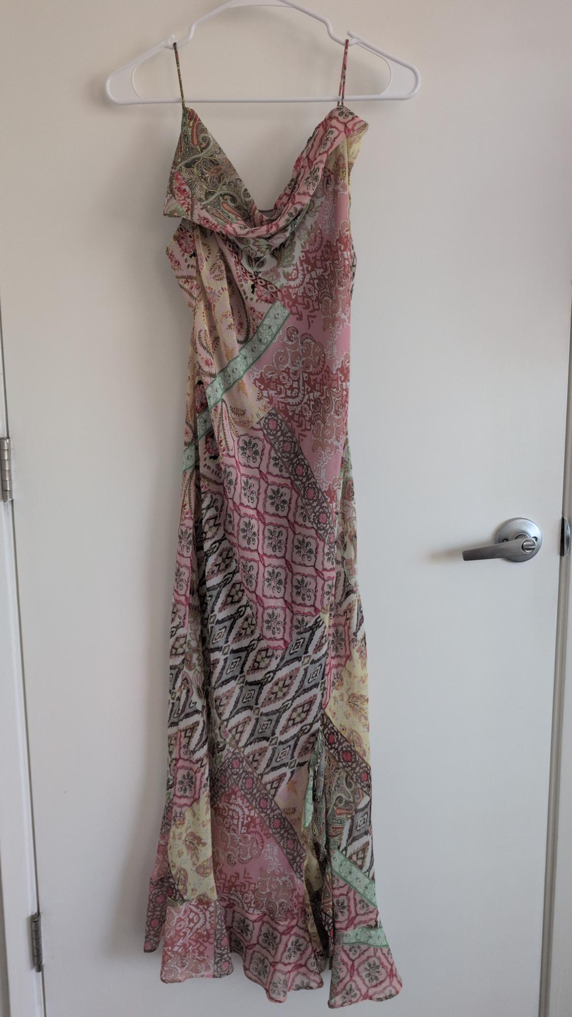 Long spaghetti-strap dress with a cowl neckline and pastel patchwork print, hanging on a white door.