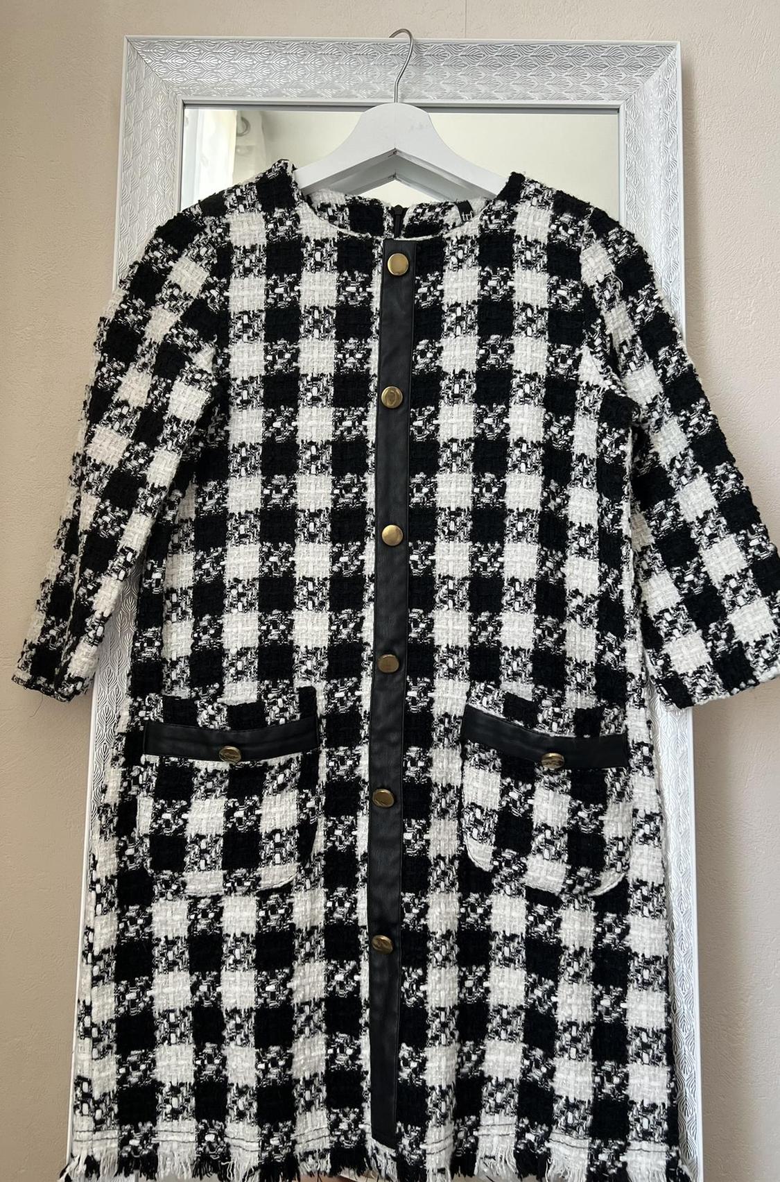 Front view of a black and white checked coat with gold buttons and side pockets.
