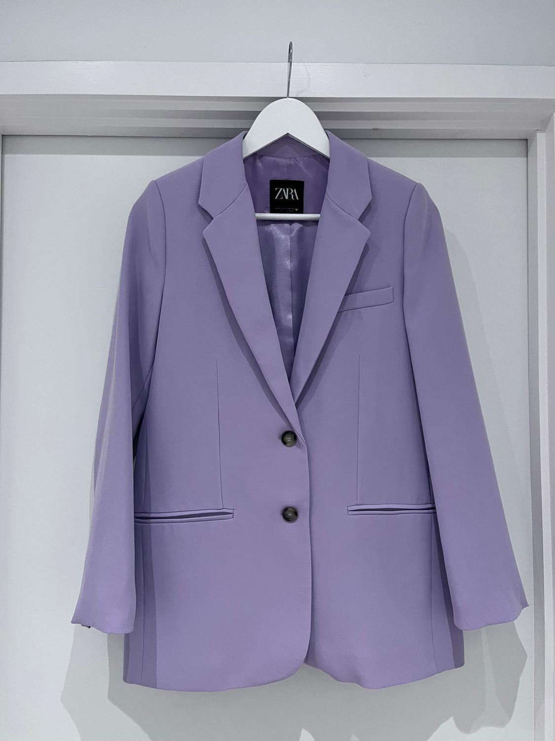 Women's purple blazer hanging on a white hanger, with two dark buttons and a Zara label visible on the collar.