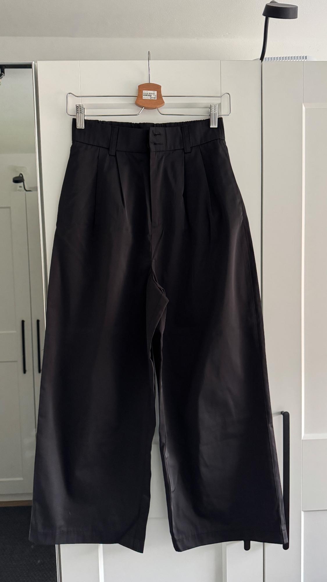Black trousers hanging on a wooden hanger over a white wardrobe. Room background with natural light.
