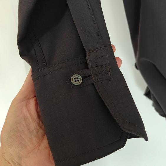 Hand holding the cuff of a black shirt with a button and visible stitching, on a white background.