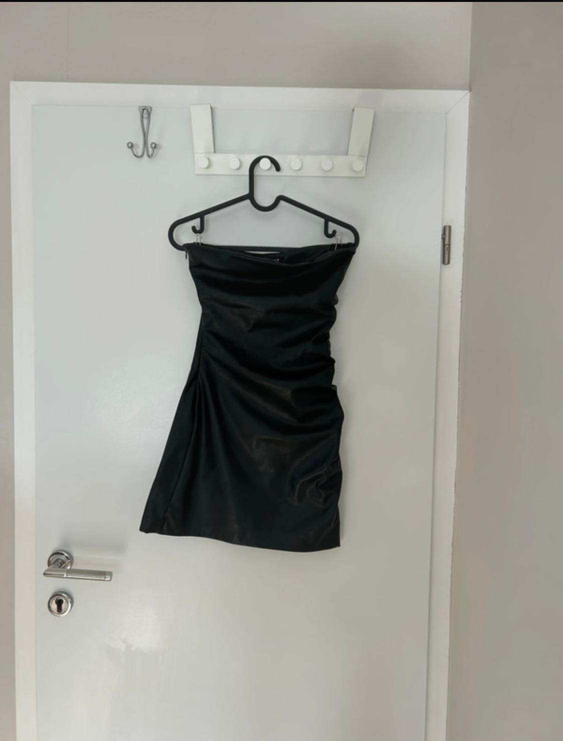 Black strapless dress hanging on a hanger over a white door with a wall hook.