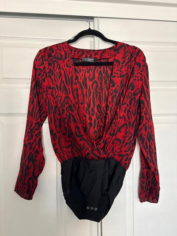 Red long-sleeved bodysuit with black print, hanging on a black hanger in front of a white door.