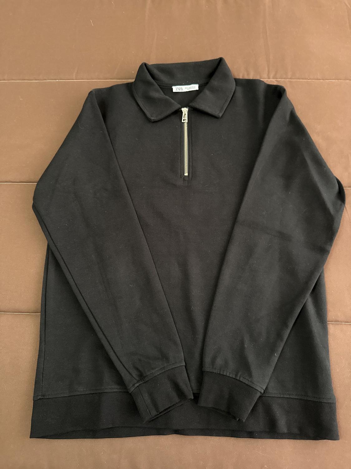 Black zip-up polo neck jumper on a brown surface. Visible label on the collar.