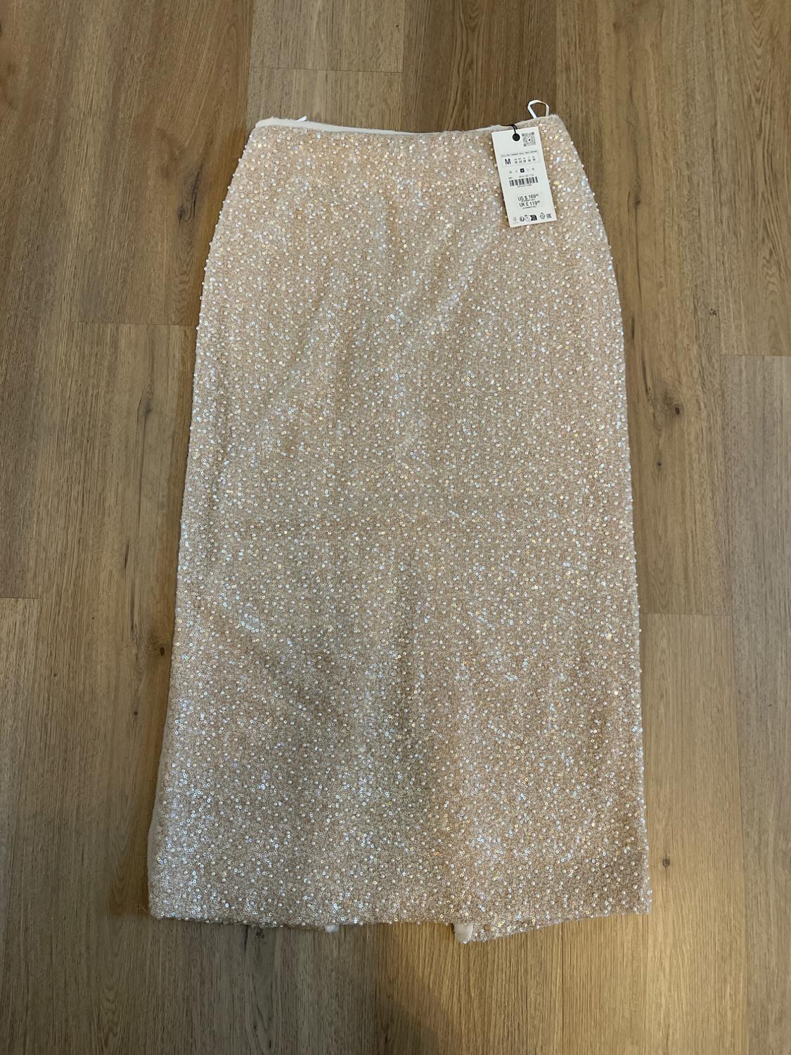 Shiny beige midi skirt on a wooden floor, with a visible price tag.