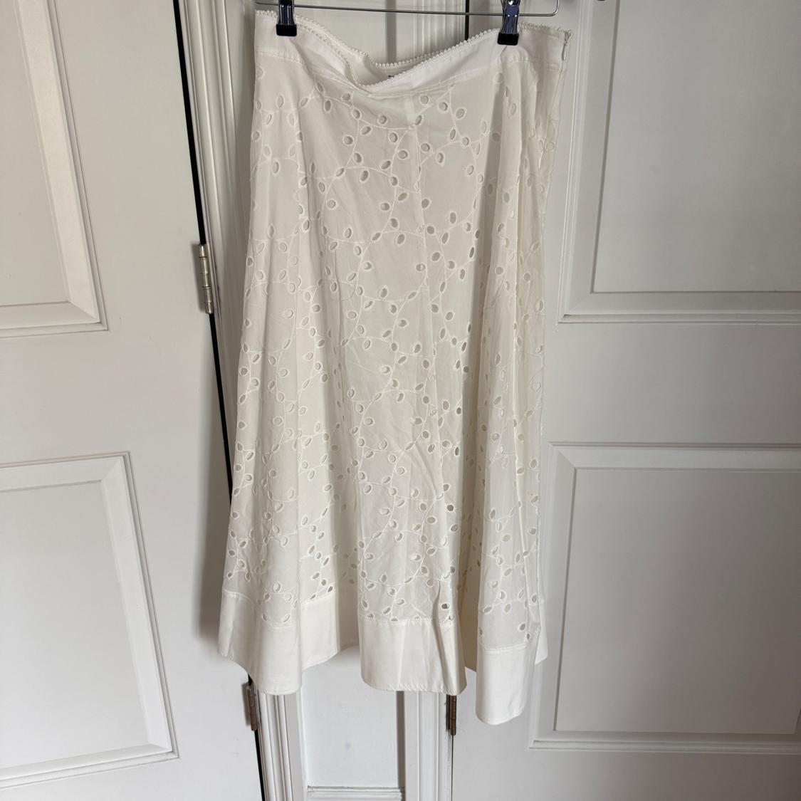 White eyelet embroidered skirt hanging on a white door. The fabric features a floral pattern design.