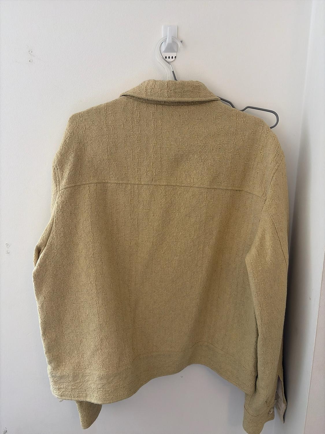 Rear view of a textured beige jacket hanging on a hanger against a plain white wall. Relaxed and minimalist atmosphere.