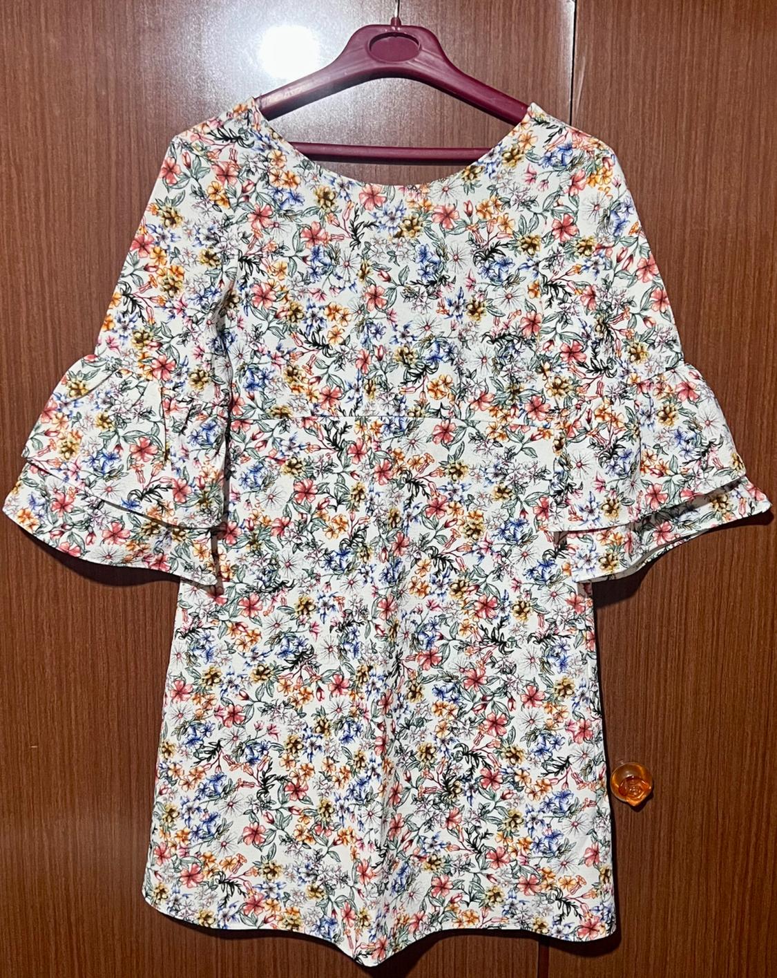 Long-sleeved floral dress with ruffles, hanging on a purple hanger over a wooden door.