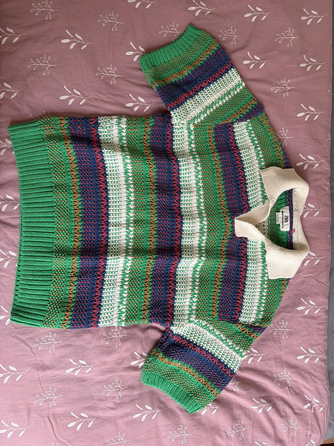 Green, blue, and white striped knit polo shirt with a white collar and ZARA tag, on a pink fabric with a leaf print.