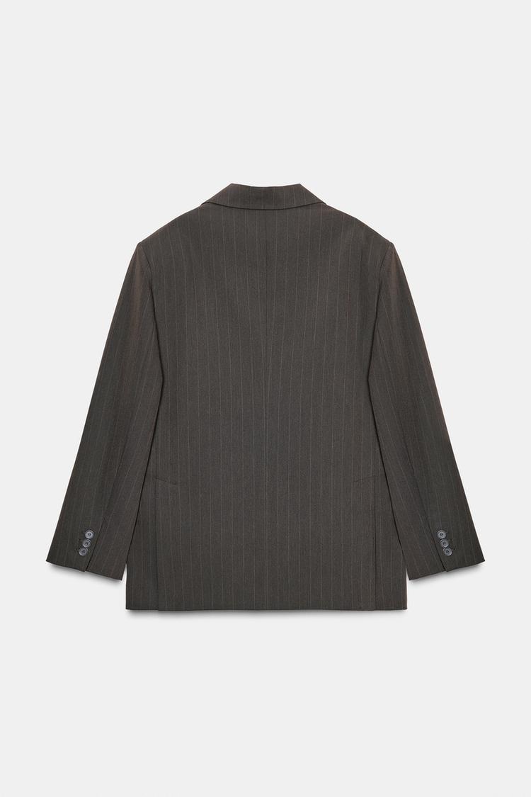 Zadnji pogled na prevelik rjav blazer z diplomatsko progo, ovratnikom in dolgimi rokavi z gumbi na manšetah.