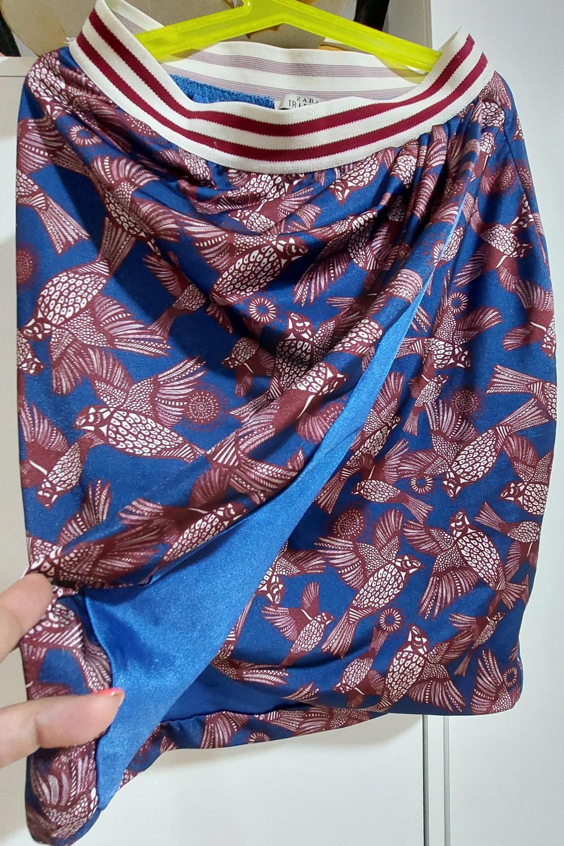 Detail of blue skirt with red bird print and striped elasticated waistband.