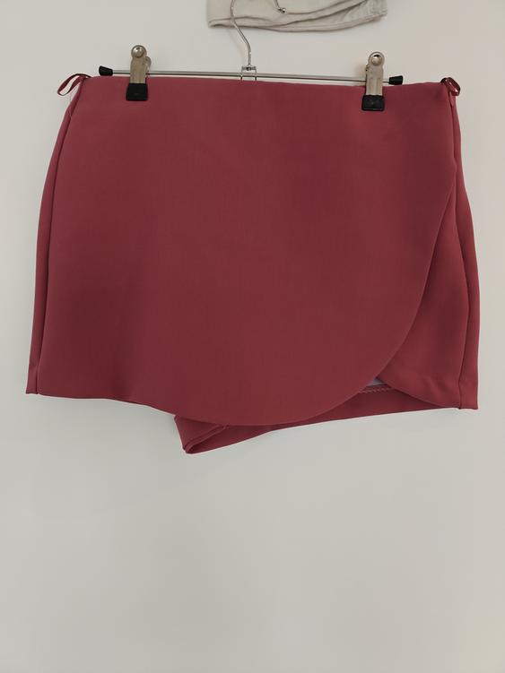 Dark red short skirt hanging on a hanger against a white background. Asymmetric hem design.