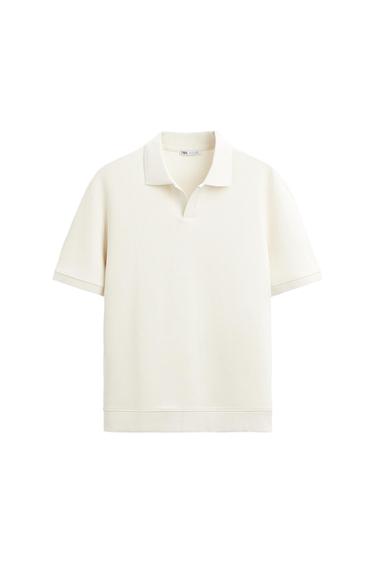 White short-sleeved polo shirt with ribbed texture and classic collar. White background. Visible internal label with text "ZARA".