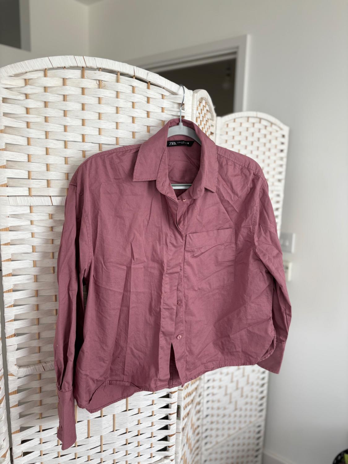 A dark pink, crumpled shirt is hanging on a white wicker screen in a well-lit interior space.