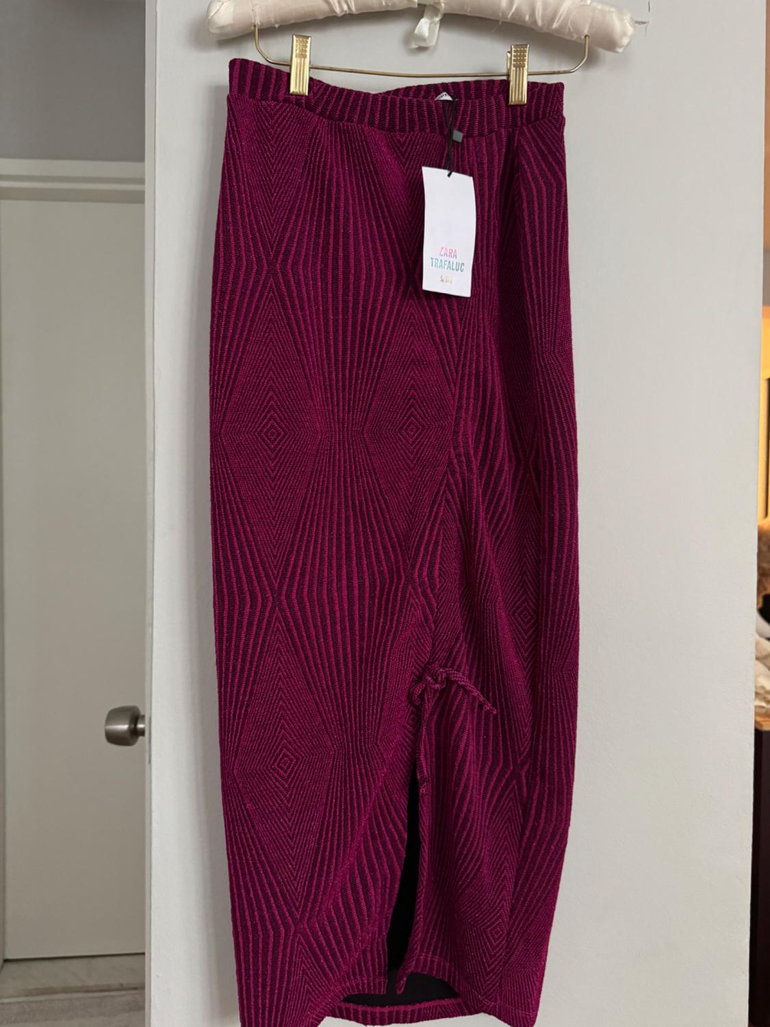 Burgundy long skirt with a geometric pattern hanging on a hanger. Visible label: "ZARA TRAFALUC". White wall background.