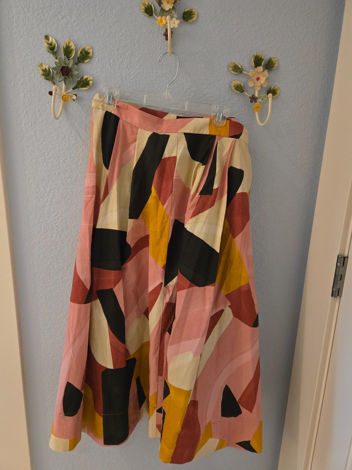 Skirt hanging on a blue wall with an abstract print in pink, black, beige, and yellow tones. Floral decorations on the wall.