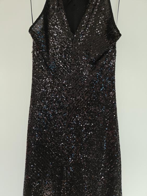 Sleeveless black dress with shiny sequins hanging on a hanger against a white background.