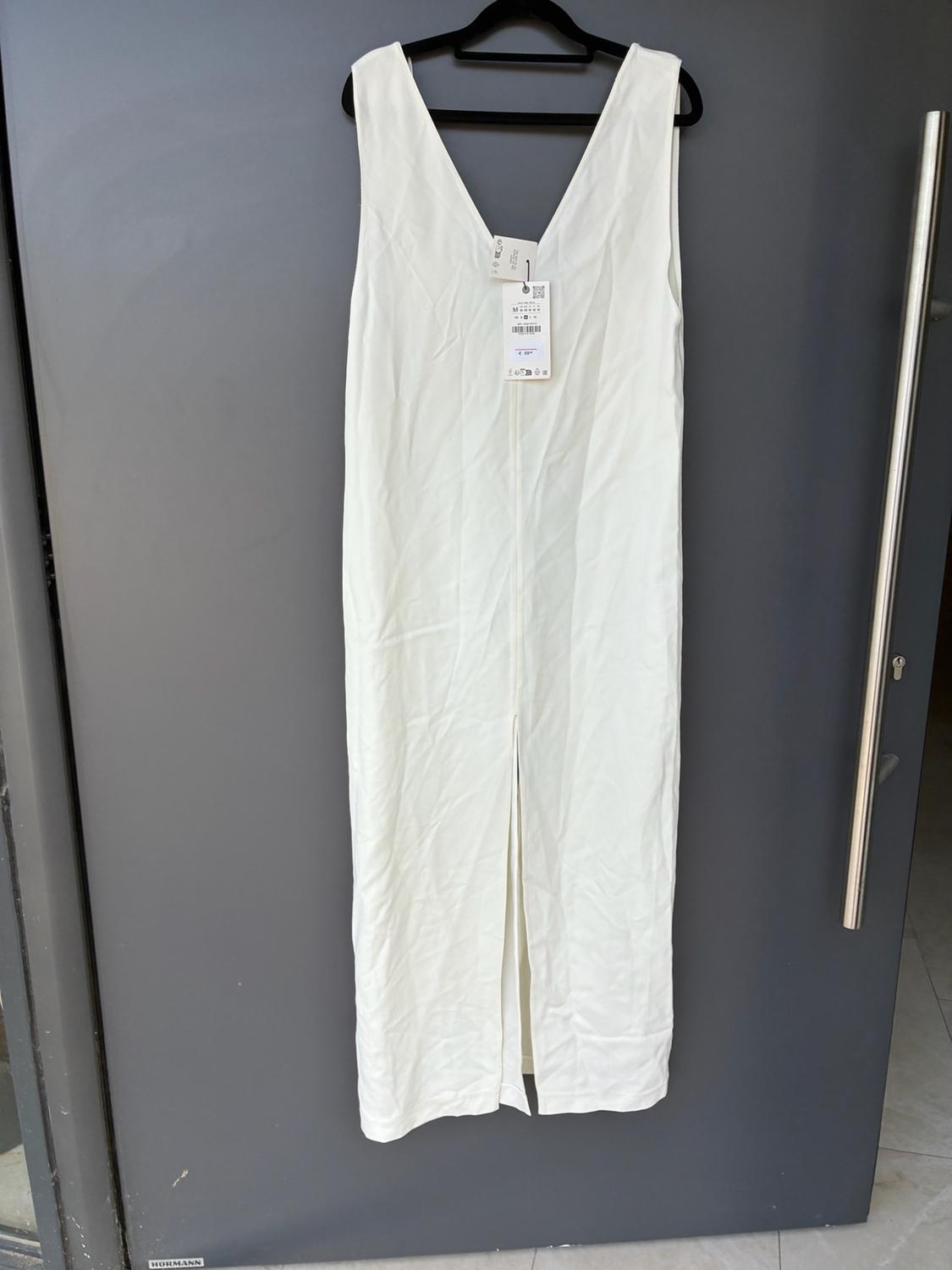Long white sleeveless dress with a V-neckline and front split, hanging on a dark grey door. Text: HORMANN.
