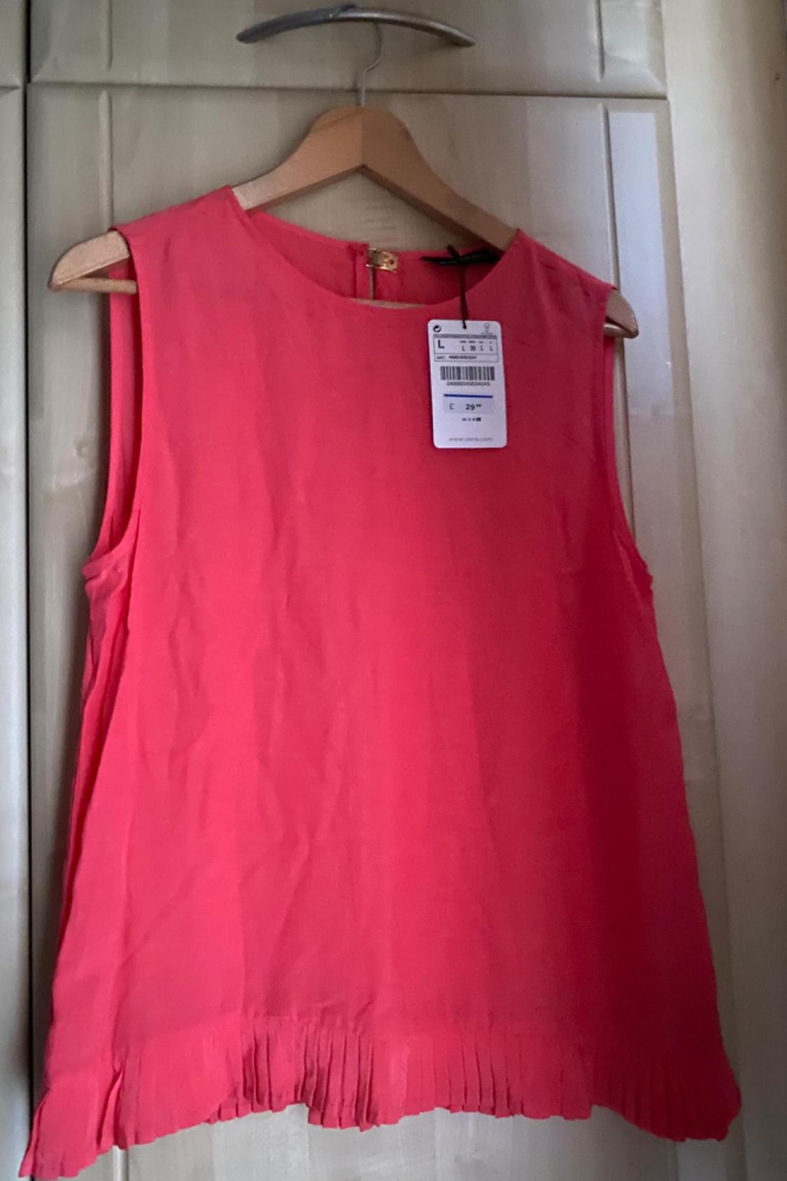Front view of pink sleeveless blouse with label and pleated hem detail.