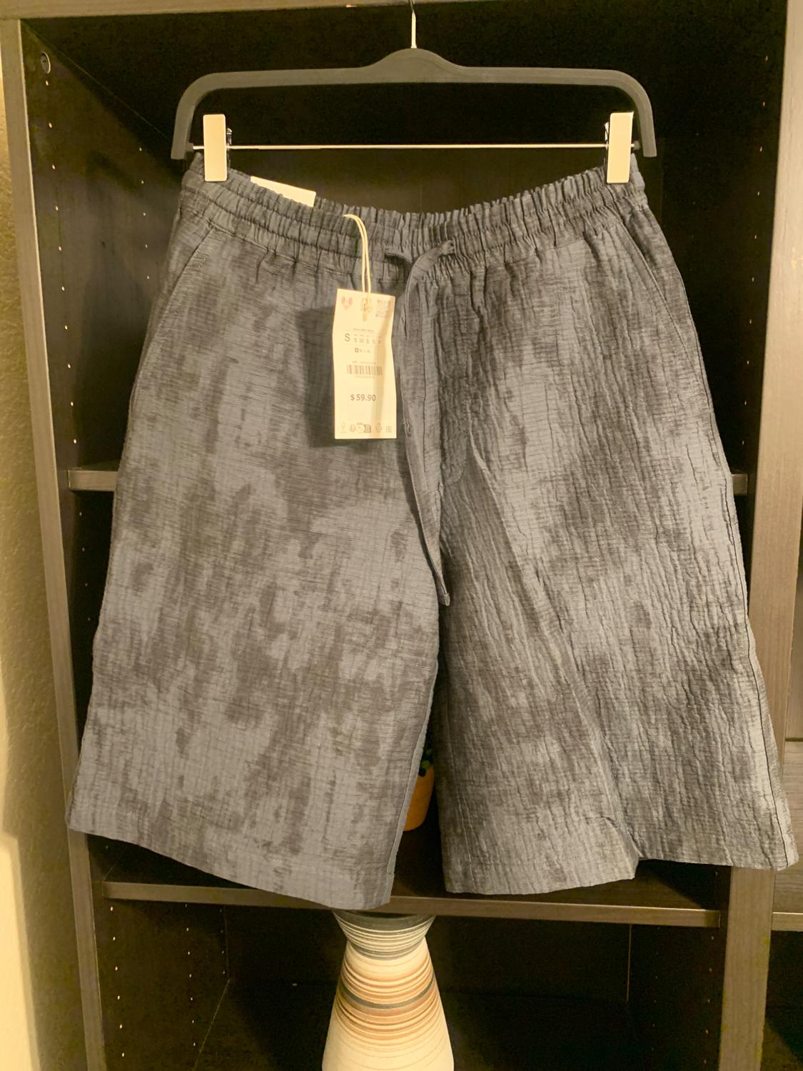 Textured grey shorts hanging on a black hanger. Visible tag with price of $59.00. Dark shelving background.
